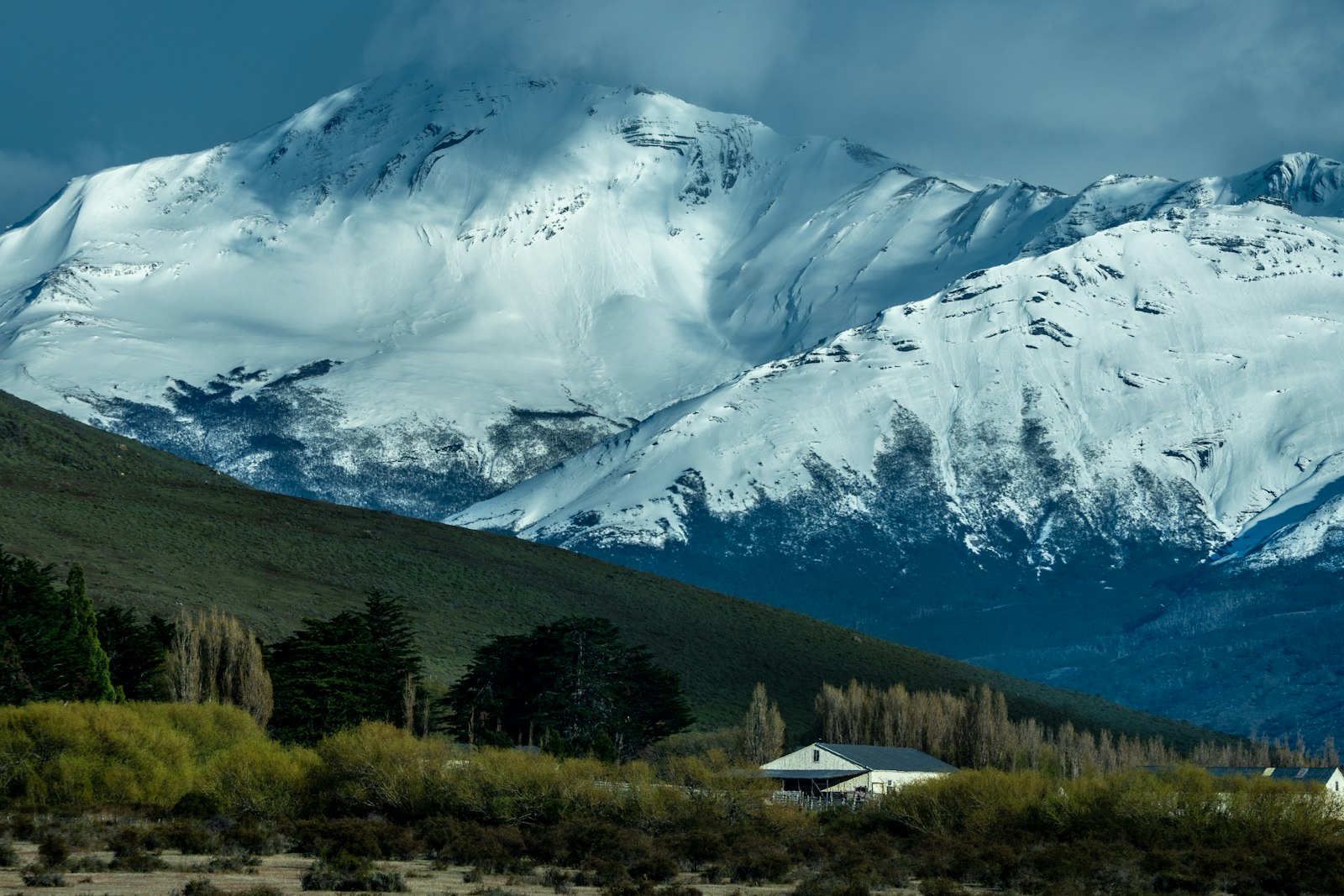 Hikers crossing a green valley beneath jagged snow-capped peaks