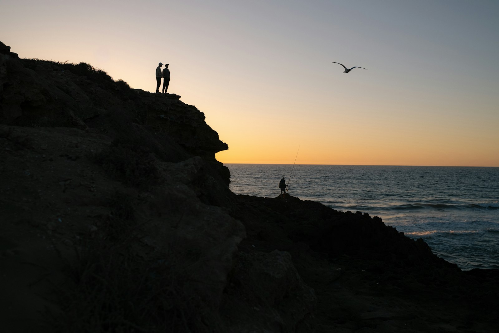 Travellers watching the sunset over a wide ocean horizon from a clifftop